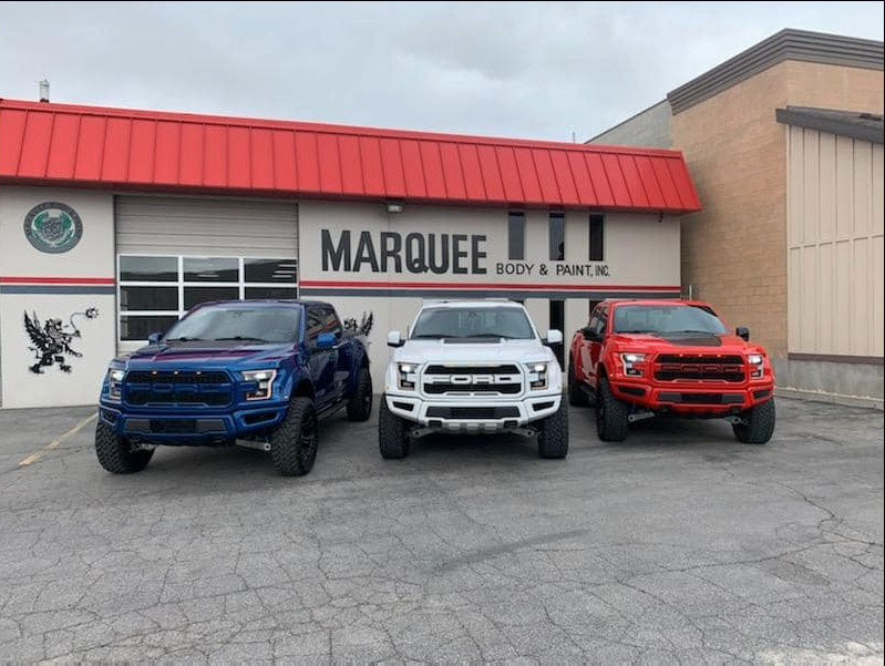 Blue White and Red pickup trucks, Raptors, parked at Marquee Body and Paint